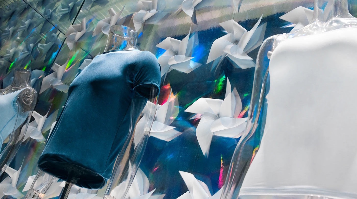 Glass mannequins in front of a wall of white folded-paper pinwheels lit with dichroic colour